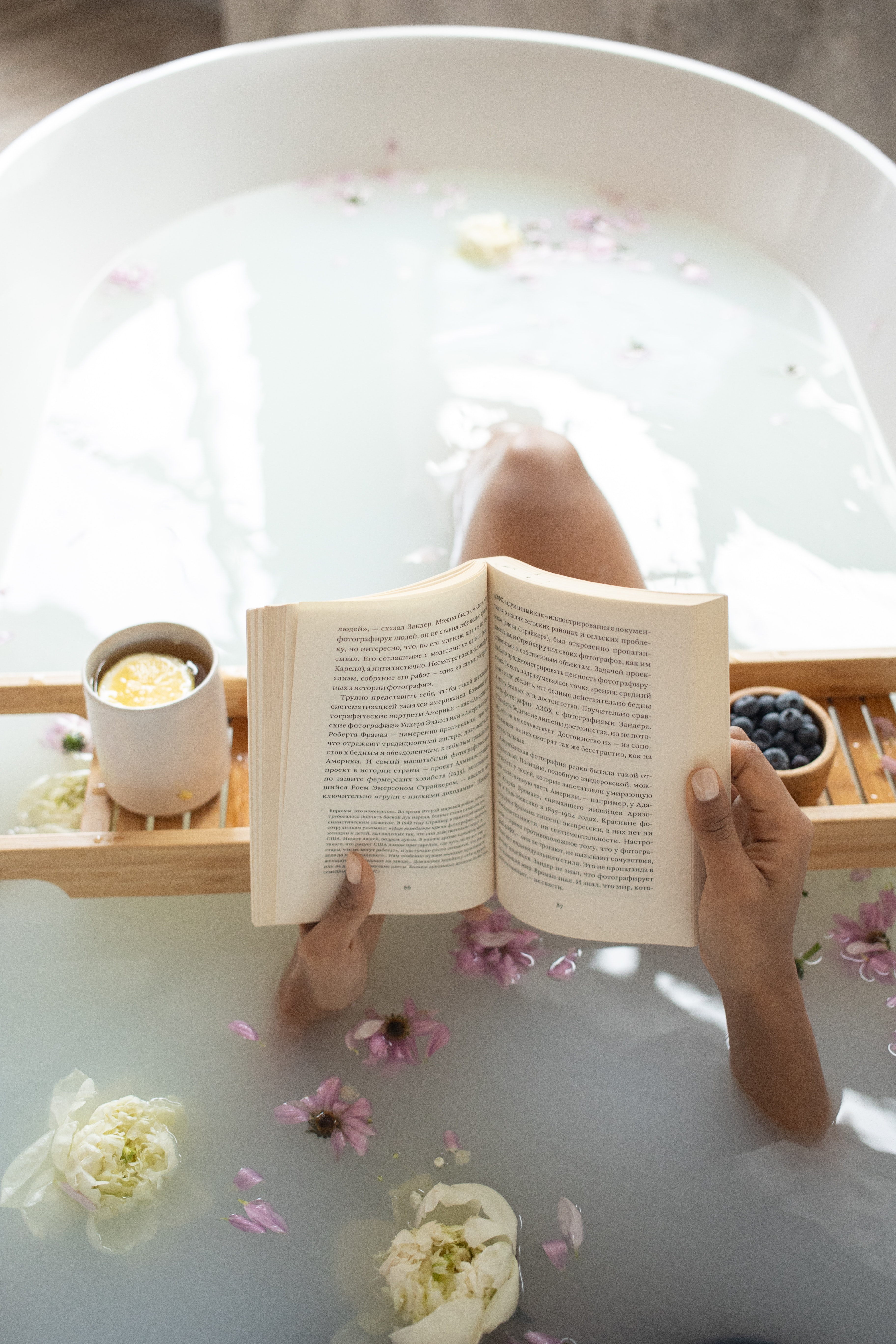 A relaxing spa bath with floating flowers and a guest reading a book.